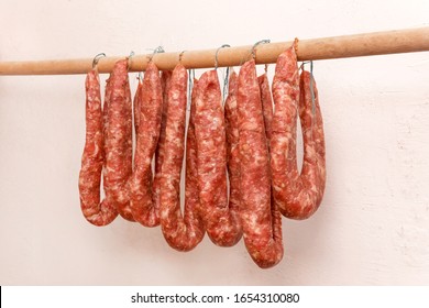 Drying Sausages From Raw Minced Meat In Limbo On A Wooden Stick On A White Wall Background At Home