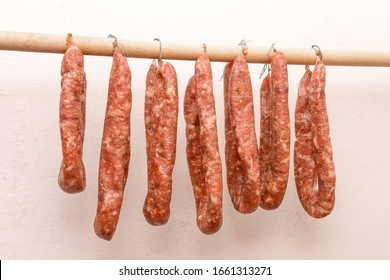 Drying Sausages From Raw Minced Meat In Limbo On A Wooden Stick On A White Wall Background At Home