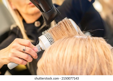 Drying Straight Blond Hair With Black Hairdryer And White Round Brush In Hairdresser Salon, Close Up