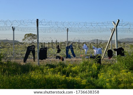 Drying washed clothes on a border fence with barbed wire. Difficult life conditions in transit refugee/migrant camp at the Greek-North Macedonian border. Families stuck on their way to Western Europe.