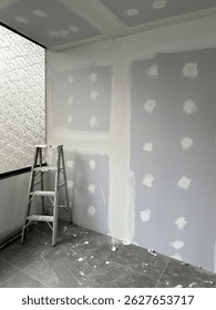 Drywall in progress with joint compound applied and a ladder standing in a corner of a renovated room.