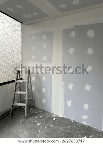 Drywall in progress with joint compound applied and a ladder standing in a corner of a renovated room.
