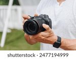dslr camera in hands, young adult caucasian photographer in white t-shirt at work outdoors in sunny summer day