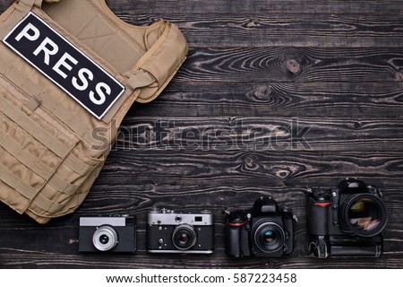 DSLR cameras,retro cameras and body armor for mass media on dark wooden table..Top view/Many cameras and body armor on wooden table