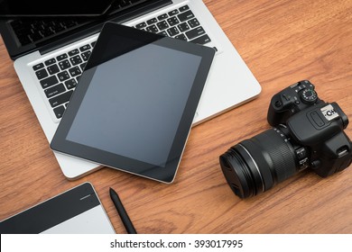 DSLR digital camera with tablet and notebook laptop on wooden desk table