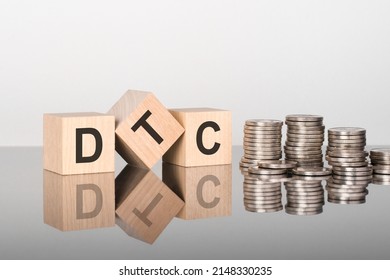 DTC - Direct to Consumer - text is made up of letters on wooden cubes lying on a mirror surface, gray background. stacks with coins. inscription is reflected from the surface. selective focus.