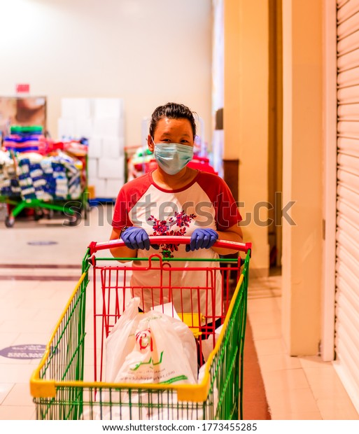 Dubai 10/7/2020 United Arab Emirates. Young\
beautiful girl with shopping cart wears medical mask and hand\
gloves against coronavirus outbreak in UAE.Shopping concept during\
covid19 pandemic.