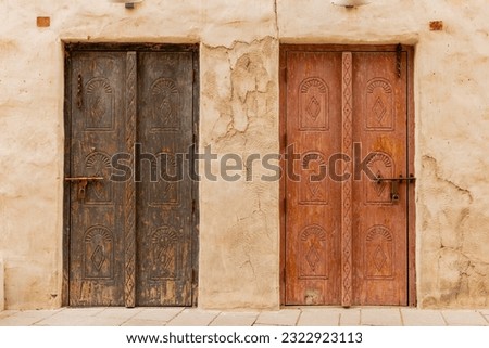 Dubai, Al Fahidi, April 2023 - Old historic district. Two ancient arabic wooden front doors with oriental pattern. Door surrounded by a clay wall.