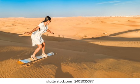 Dubai desert sand dunes, an Asian woman on Dubai desert safari, United Arab Emirates vacation, woman on vacation in Dubai sandboarding at the sand dunes of Dubai  - Powered by Shutterstock