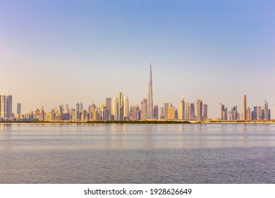 Dubai Downtown skyline landscape with reflections in Dubai Creek, warm golden colors, seen from Dubai Creek Harbour promenade.