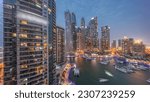 Dubai marina tallest skyscrapers with glowing windows and yachts in harbor aerial night after sunset. View at apartment buildings, hotels and office blocks, modern residential development of UAE