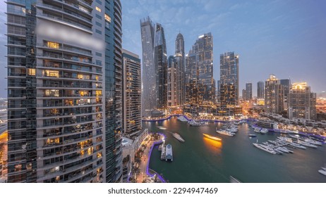 Dubai marina tallest skyscrapers with glowing windows and yachts in harbor aerial night after sunset. View at apartment buildings, hotels and office blocks, modern residential development of UAE