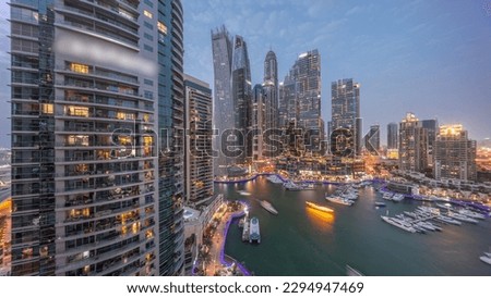 Dubai marina tallest skyscrapers with glowing windows and yachts in harbor aerial night after sunset. View at apartment buildings, hotels and office blocks, modern residential development of UAE