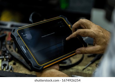 DUBAI / UAE - 07 05 2018: Mechanic Uses A Tablet To Diagnose Faults In An Auto Repair Shop. Heavy Duty, Tough Tablet Like Ipad, Tools Cars In Background