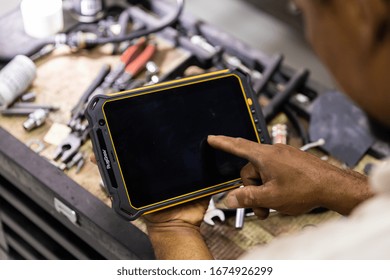 DUBAI / UAE - 07 05 2018: Mechanic Uses A Tablet To Diagnose Faults In An Auto Repair Shop. Heavy Duty, Tough Tablet Like Ipad, Tools Cars In Background