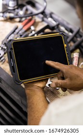 DUBAI / UAE - 07 05 2018: Mechanic Uses A Tablet To Diagnose Faults In An Auto Repair Shop. Heavy Duty, Tough Tablet Like Ipad, Tools Cars In Background