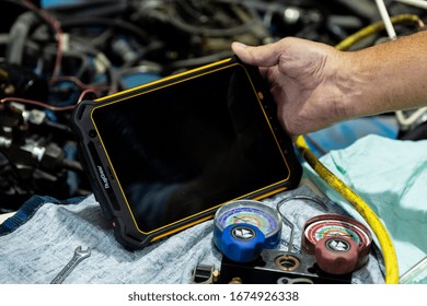 DUBAI / UAE - 07 05 2018: Mechanic Uses A Tablet To Diagnose Faults In An Auto Repair Shop. Heavy Duty, Tough Tablet Like Ipad, Tools Cars In Background