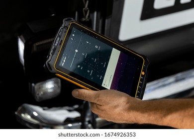 DUBAI / UAE - 07 05 2018: Mechanic Uses A Tablet To Diagnose Faults In An Auto Repair Shop. Heavy Duty, Tough Tablet Like Ipad, Tools Cars In Background