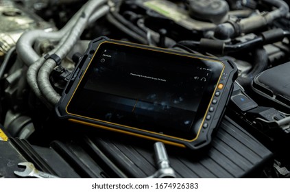 DUBAI / UAE - 07 05 2018: Mechanic Uses A Tablet To Diagnose Faults In An Auto Repair Shop. Heavy Duty, Tough Tablet Like Ipad, Tools Cars In Background