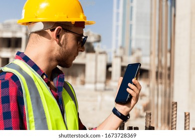 Dubai, UAE - APRIL, 07, 2019: Man On Dubai Construction Site Uses Technology To Do His Job, Smartphone Smart Phone, Wearing Hard Hat And Hi Vis Jacket, Under Dubai Skyline, Construction Worker