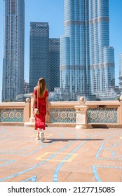Dubai, UAE. February 10, 2022. Young sexy lady in a red dress exploring Burj Khalifa skyscraper near the fountains on a hot sunny day.