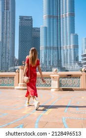 Dubai, UAE. February 10, 2022. Young sexy lady in a red dress exploring Burj Khalifa skyscraper near the fountains on a hot sunny day.