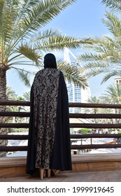 Dubai, UAE - February 18, 2018: Low Angle View Of Young Arab Woman Wearing A Modern Abaya And Facing Burj Al Arab. Fashion Concept.