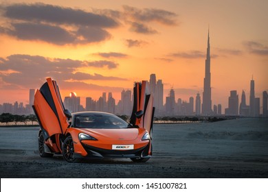 Dubai / UAE - January 29, 2019: Orange McLaren 570S car in Dubai skyline background at the sunset 