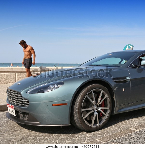 DUBAI, UAE - NOVEMBER 23,\
2017: Man walks by Aston Martin Vantage in Dubai, United Arab\
Emirates. Dubai city has a car ownership rate of 541 cars per 1,000\
population.