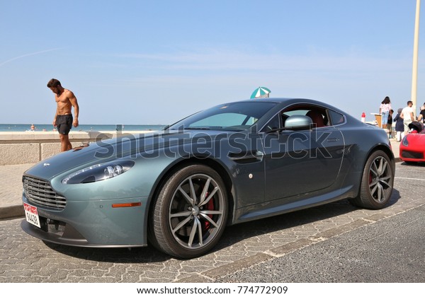 DUBAI, UAE - NOVEMBER 23,\
2017: Man walks by Aston Martin Vantage in Dubai, United Arab\
Emirates. Dubai city has a car ownership rate of 541 cars per 1,000\
population.