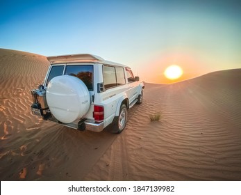 Dubai, United Arab Emirates - 10/30/2020: A Classic Retro 1990s Super Safari Nissan Patrol Driving Up A Sand Dune At Sunset In The Arabian Desert