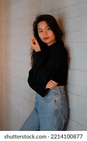 Dubai, United Arab Emirates - 2 February 2018: Southeast Asian Woman Wearing Dark Sweater And Light Jeans, Leans On A Wall And Gives The Camera A Pointed Look. Female Has Long Wavy Hair And Red Nails.