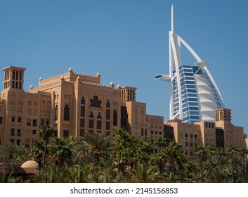 Dubai, United Arab Emirates – 4 6 2022: Burj Al Arab’s Modern Design Contrasts With The Traditional Arabic Style Of Souk Madinat In Jumeirah, Dubai, With Its Palm-lined Walkways. Clear Blue Sky. 