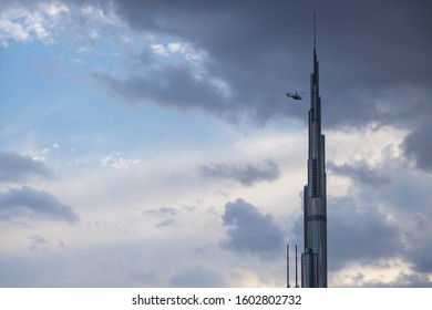 DUBAI, UNITED ARAB EMIRATES, CIRCA 2019: Burj Khalifa close up with cloudy sky in the background and helicopter flying very close to the tower. Rare cloud formation over UAE sky
