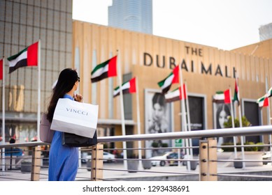 Dubai, United Arab Emirates - March 26, 2018: Asian Tourist In Front Of Dubai Mall Main Entrance With Shopping Bags