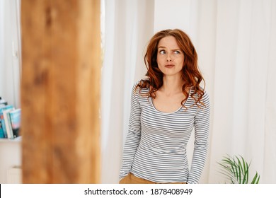 Dubious young woman pulling a wry face grimacing and looking up to the side with a thoughtful expression indoors at home with copyspace - Powered by Shutterstock