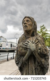 Dublin, Ireland - August 7, 2017: Great Irish Famine Bronze Statue Set On Custom House Quay Along Liffey River In Docklands. One Slender Female Figure. Green Trees.