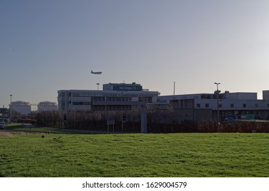 DUBLIN, IRELAND - JANUARY 15, 2020: Exterior Of The Aer Lingus Building With Landing Aer Lingus Aircraft Above In The Background. Dublin Airport. Green Lawn In The Foreground.