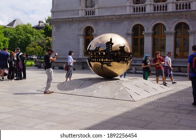 Dublin, Ireland - July 12 2014: people admiring Sphere Within Sphere (sfera con sfera) by Italian artist Arnaldo Pomodoro at the Berkeley Library, Trinity College