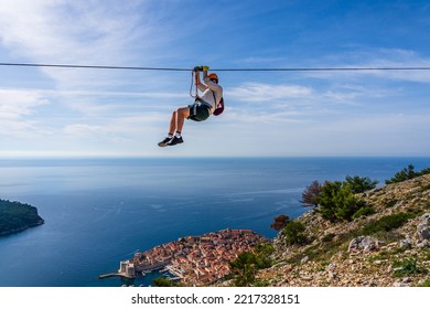 Dubrovnik, Croatia - October 2022: Unidentifiable Man Ziplining Above Dubrovnik Old Town; Thrill Seeking Holiday Adventure; Extreme Sport; Panoramic View Of The Old Town And Adriatic Sea