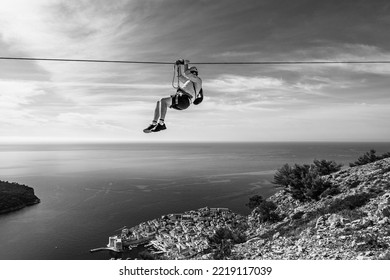 Dubrovnik, Croatia - October 2022: Unknown Man Ziplining Above Dubrovnik Old Town; Thrill Seeking Holiday Adventure; Extreme Sport; Panoramic View Of The Old Town And Adriatic Sea In Black And White