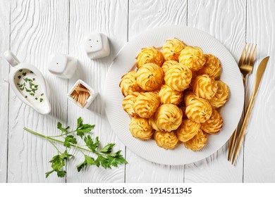 Duchess potatoes, mashed potatoes piped in decorative swirls, browned in an oven served with white sauce on a white plate on a wooden table with golden cutlery - Shutterstock ID 1914511345