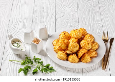 Duchess potatoes, mashed potatoes piped in decorative swirls, browned in an oven served with white sauce on a white plate on a wooden table with golden cutlery, free space - Shutterstock ID 1915135588