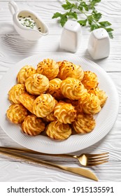 Duchess potatoes, mashed potatoes piped in decorative swirls, browned in an oven served with white sauce on a white plate on a wooden table with golden cutlery, vertical view - Shutterstock ID 1915135591