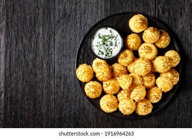 Duchess potatoes, mashed potatoes piped in decorative swirls, browned in an oven served with white sauce on a black plate, flat lay, free space - Shutterstock ID 1916964263