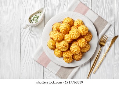 Duchess potatoes, mashed potatoes piped in decorative swirls, browned in an oven served with white sauce on a white plate on a wooden table with golden cutlery, flat lay - Shutterstock ID 1917768539