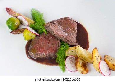 duck breast in a red sauce with baked potatoes and radishes on white plate - Shutterstock ID 1021636516