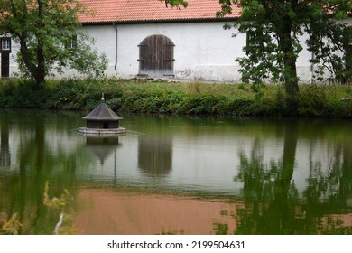 Duck house on a lake with a white building. refelctions of the building and trees in the green water of the lake
