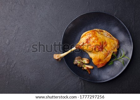 Duck leg confit with mushroom sauce on black plate. Slate background. Copy space. Top view.