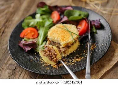 
duck shepherd's pie  with mesclun salad on a modern black plate on wooden tabl
